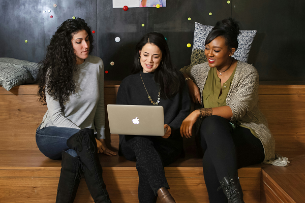 Three Women Looking At Laptop On Bench