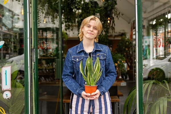 Woman In Shop Door Holding Plant